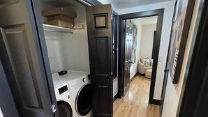 Une buanderie équipée d’un lave-linge et d’un sèche-linge, avec un plancher en bois et une porte donnant sur une autre pièce.