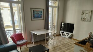 A living room with a black leather sofa, a red armchair, a white table, and a TV stand. - Newly renovated apartment Joliette Marseille (Marseille)