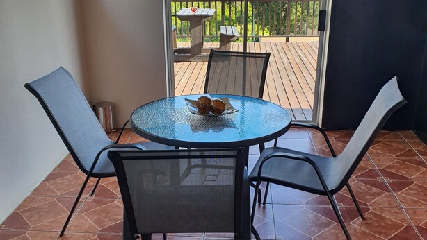 Een terras met een ronde tafel en vier stoelen, een schuifdeur die uitkomt op een terras, en een betegelde vloer.