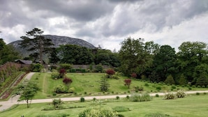 Um jardim bem cuidado, com gramados aparados, um caminho sinuoso e uma montanha ao fundo.