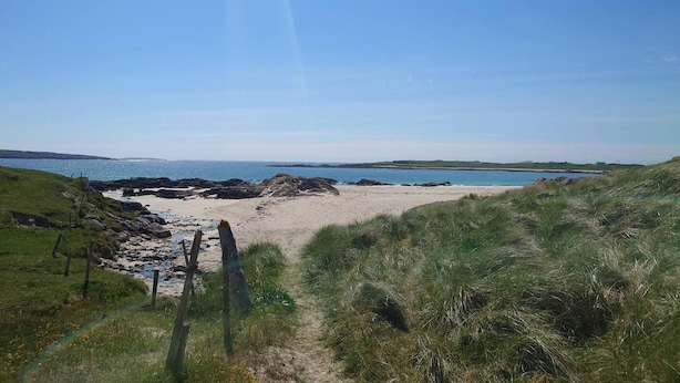 Paisagem costeira com uma praia de areia, dunas gramadas e um céu azul límpido.