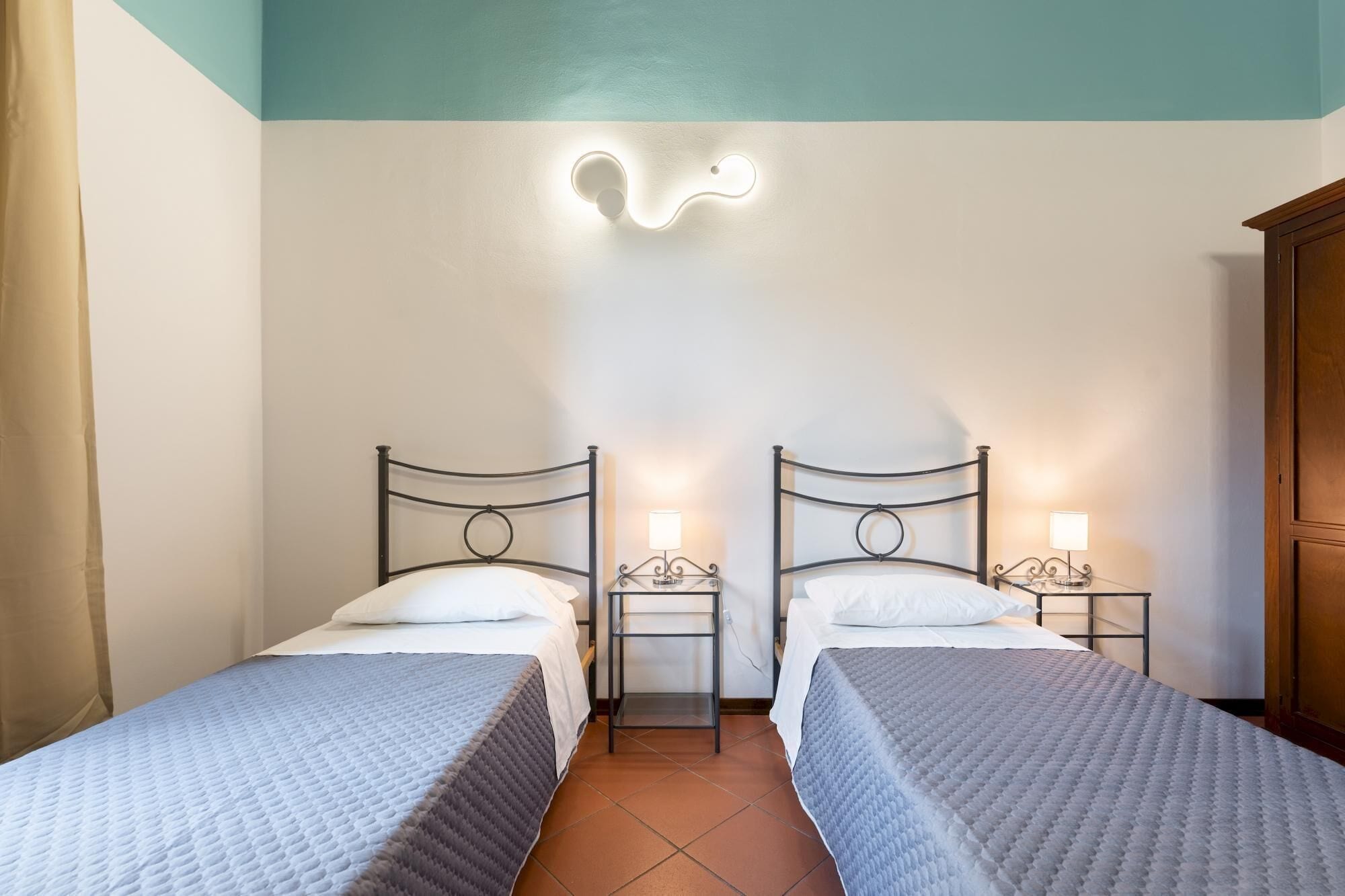 A room with two beds, each with a nightstand and a wall-mounted light fixture.
