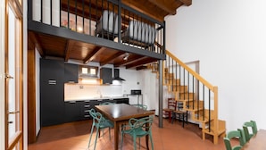 A kitchen with a dining area, featuring a wooden staircase, black cabinets, and green chairs. - Appartamento Via Dell Oriuolo (Florence)