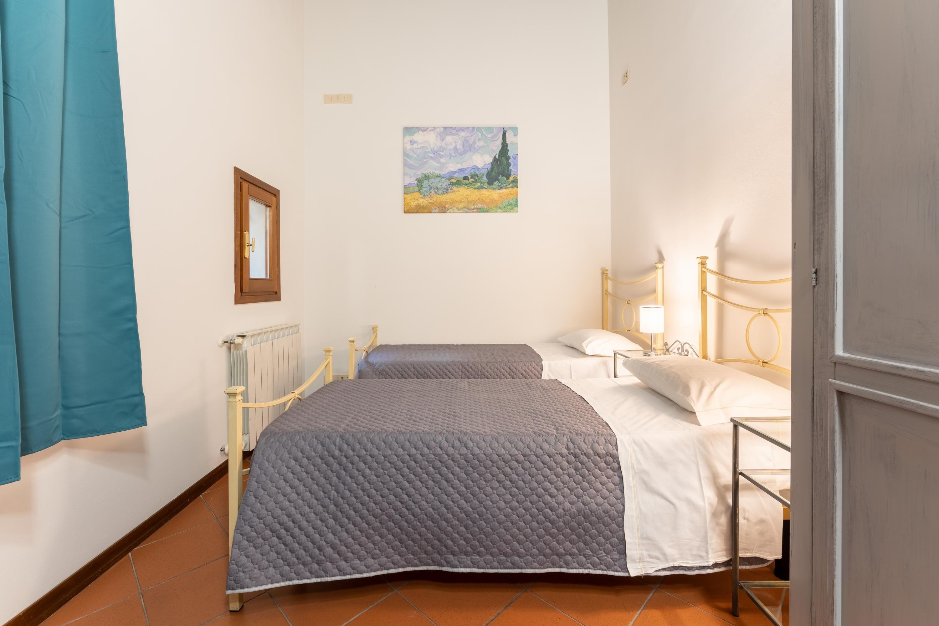 Ein Schlafzimmer mit zwei Betten, einem Heizkörper, einem Bild an der Wand und einem blauen Vorhang.