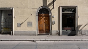A building with a wooden door, a shop with a sign reading "TRATTORIA Cucina Toscana", and a closed shutter with graffiti. - Appartamento Via Dell Oriuolo (Florence)