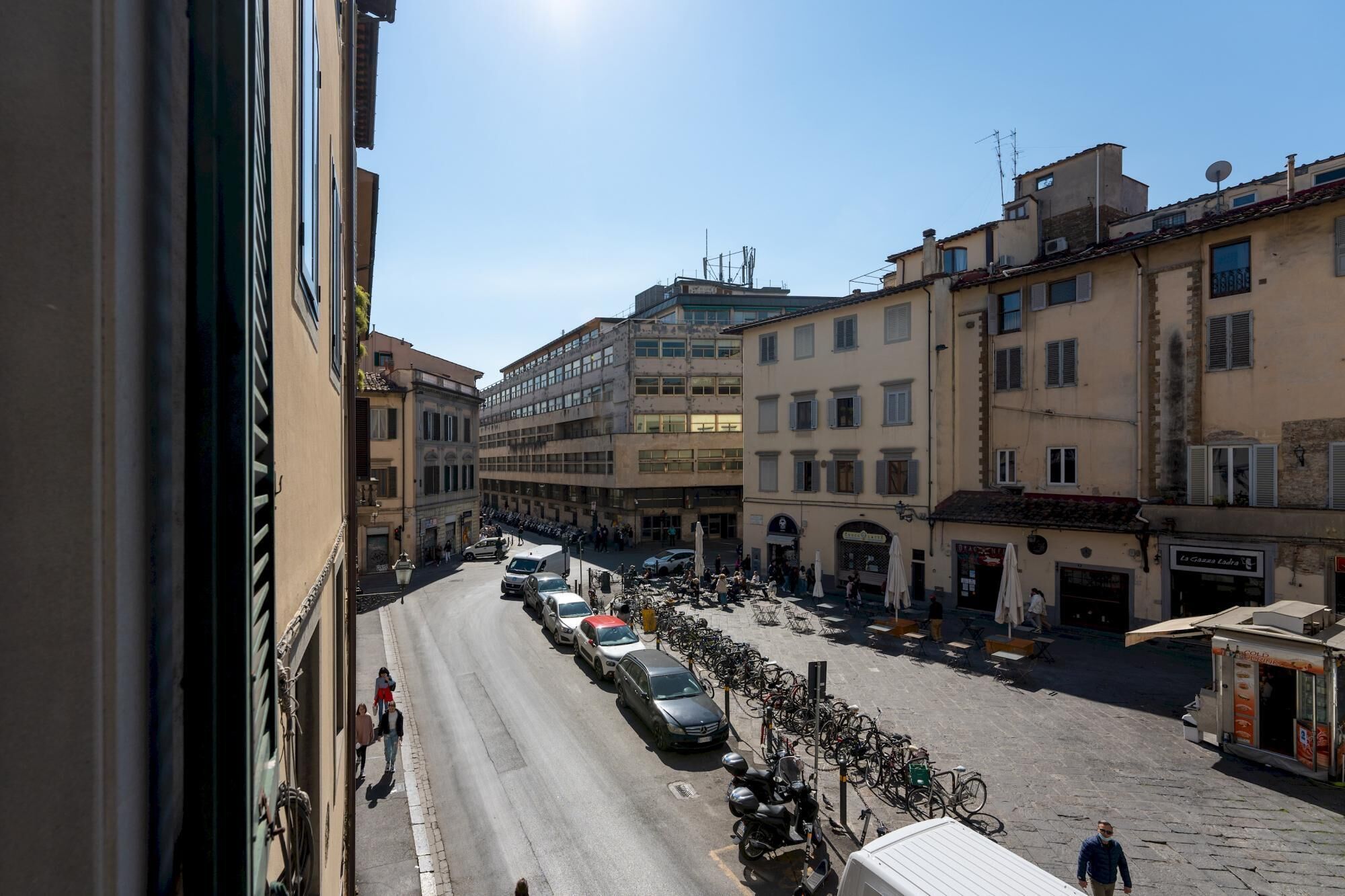 A street view with parked cars and bicycles, buildings with balconies, and a clear sky.
