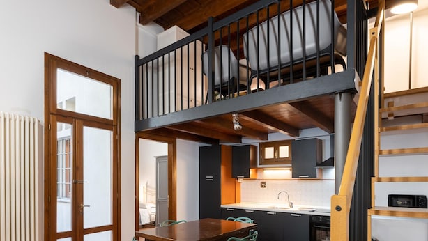 A dining area with a wooden table and chairs, a kitchen with a sink and cabinets, and a staircase leading to an upper level. - Appartamento Via Dell Oriuolo (Florence)