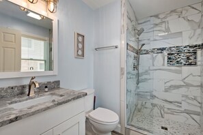 A bathroom with a marble sink, a toilet, and a glass-enclosed shower with marble tiles.