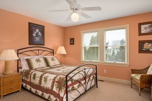 Une chambre à coucher comprenant un lit, une table de chevet, une lampe, un ventilateur de plafond et une fenêtre avec des stores.