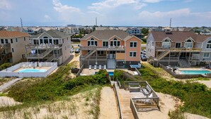 A beachfront property with multiple houses, a swimming pool, and a wooden deck. - Barefootin'- Oceanfront, private pool, hot tub, pool table, private walkway to the beach! (Nags Head)