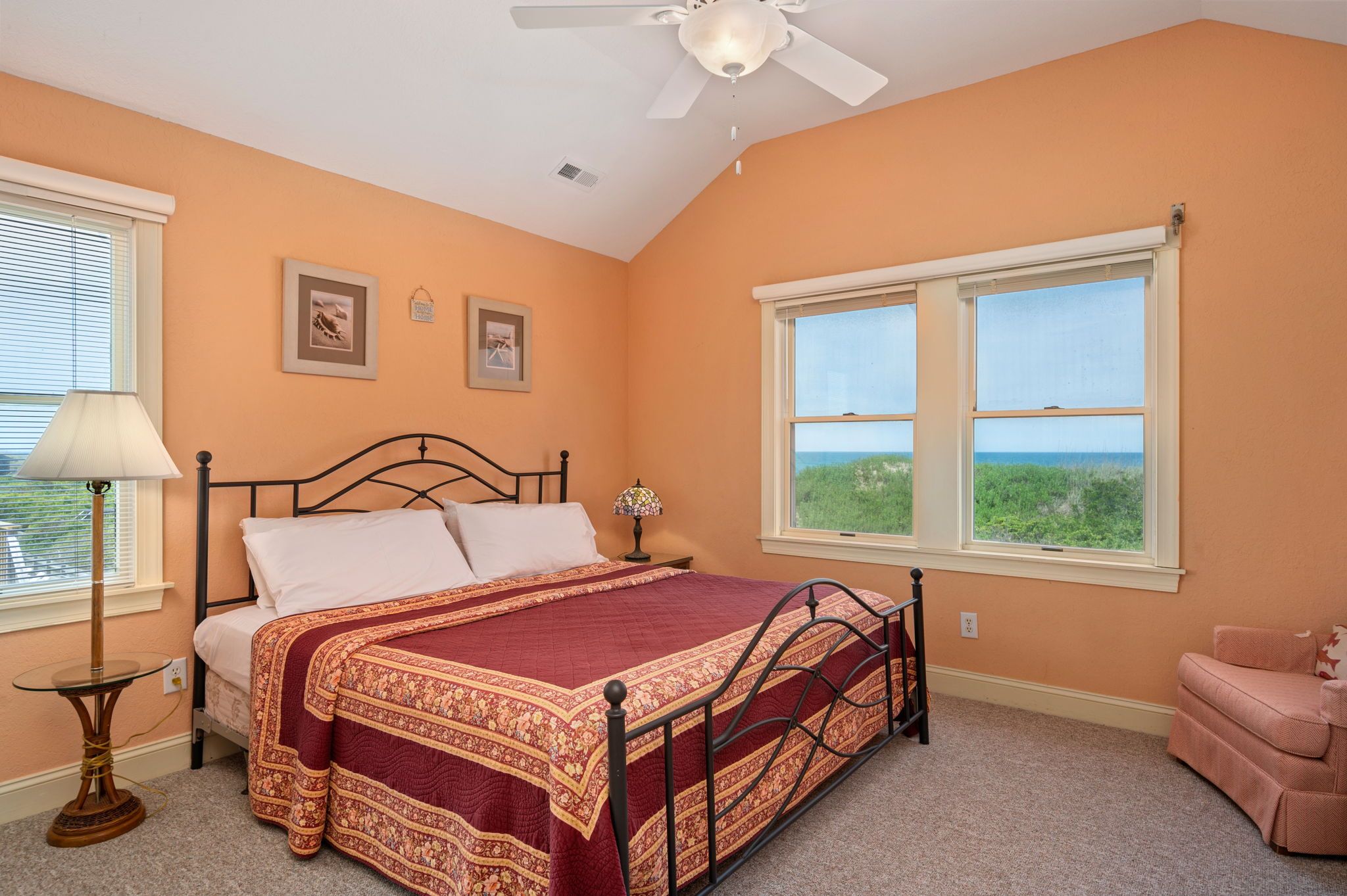 A bedroom with a bed, a window with a view, a ceiling fan, and a nightstand.