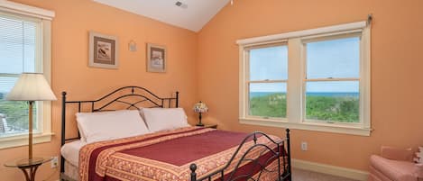 A bedroom with a bed, a window with a view, a ceiling fan, and a nightstand.