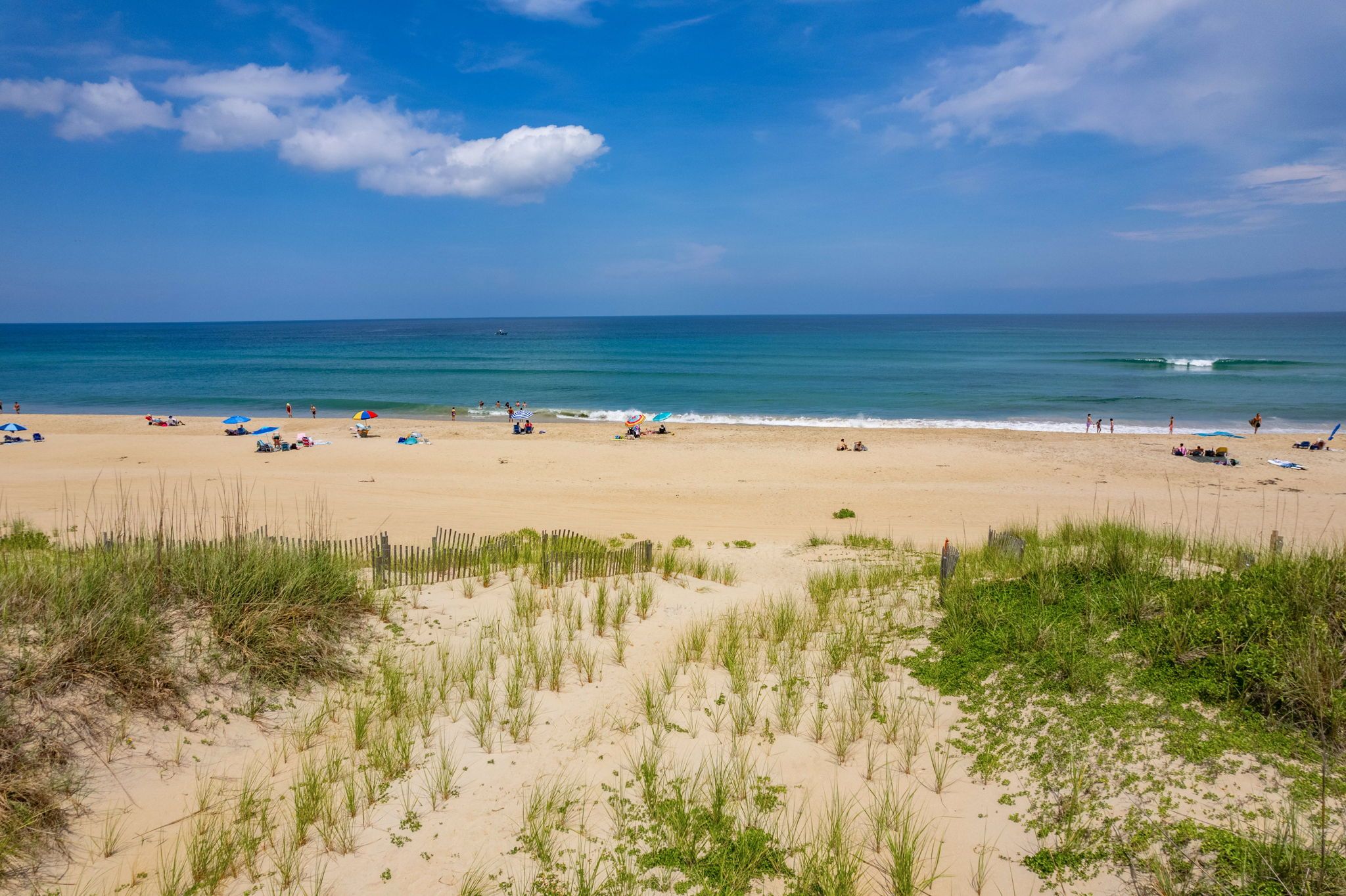 Ein Strand mit Dünen, einem Holenzaun und dem Meer im Hintergrund.