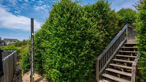 A wooden staircase leading up to a wooden deck, surrounded by dense green foliage. - Barefootin'- Oceanfront, private pool, hot tub, pool table, private walkway to the beach! (Nags Head)