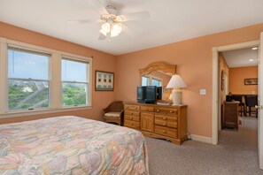 A bedroom with a bed, dresser, television, and a view of greenery outside. - Barefootin'- Oceanfront, private pool, hot tub, pool table, private walkway to the beach! (Nags Head)