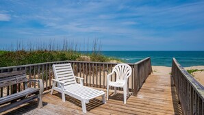 A wooden deck with two white lounge chairs and a bench, overlooking a beach and ocean. - Barefootin'- Oceanfront, private pool, hot tub, pool table, private walkway to the beach! (Nags Head)