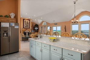 A kitchen with a large island, a refrigerator, and a dining area with chairs.