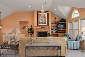 A cozy living room with a fireplace, a ceiling fan, and a large window. - Barefootin'- Oceanfront, private pool, hot tub, pool table, private walkway to the beach! (Nags Head)
