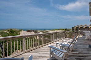 A wooden deck with white chairs overlooking a beach.