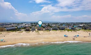 Una zona costera con casas frente a la playa, una playa de arena y olas del océano.