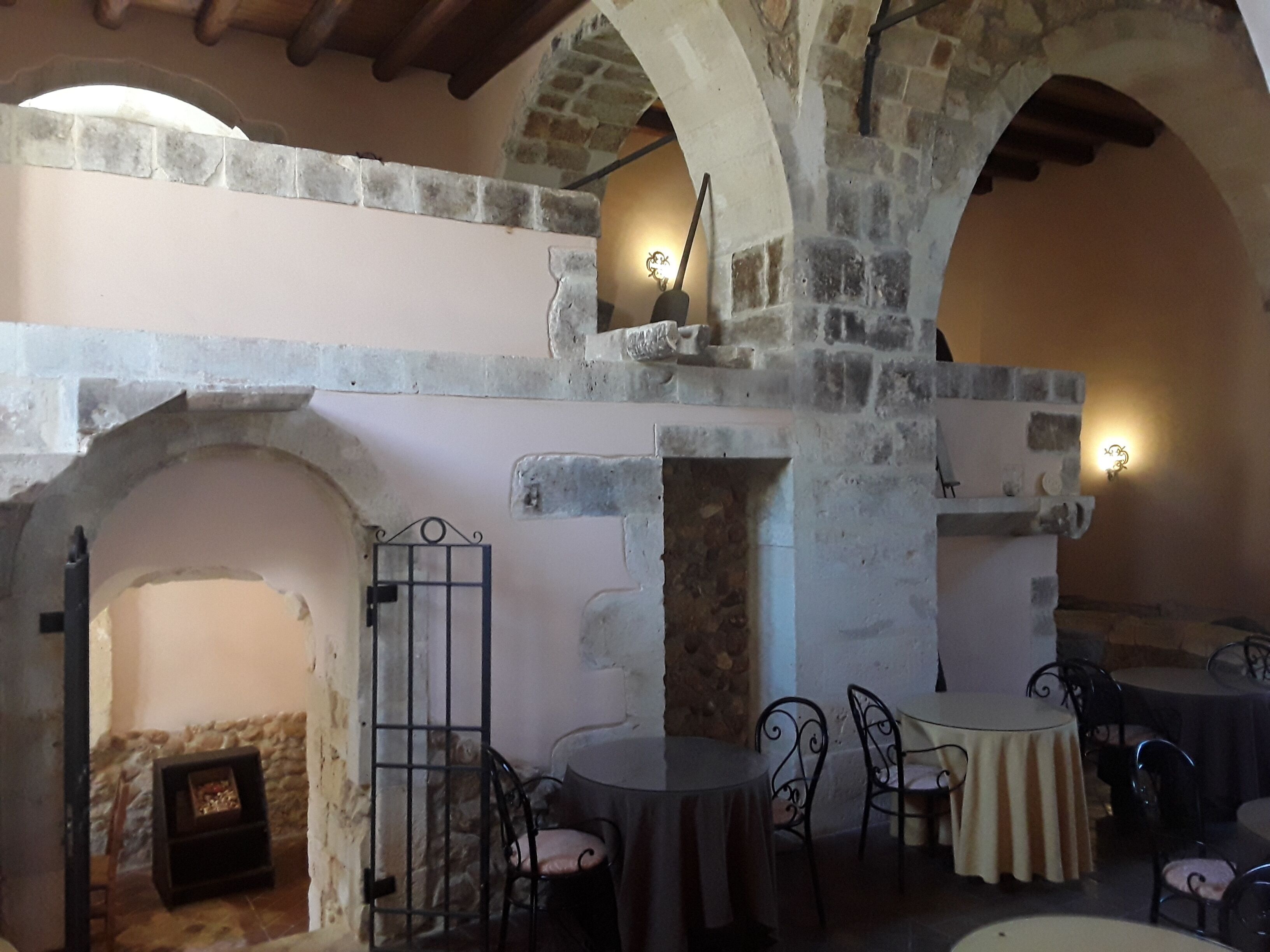 A rustic interior with stone arches, a fireplace, and tables with chairs.