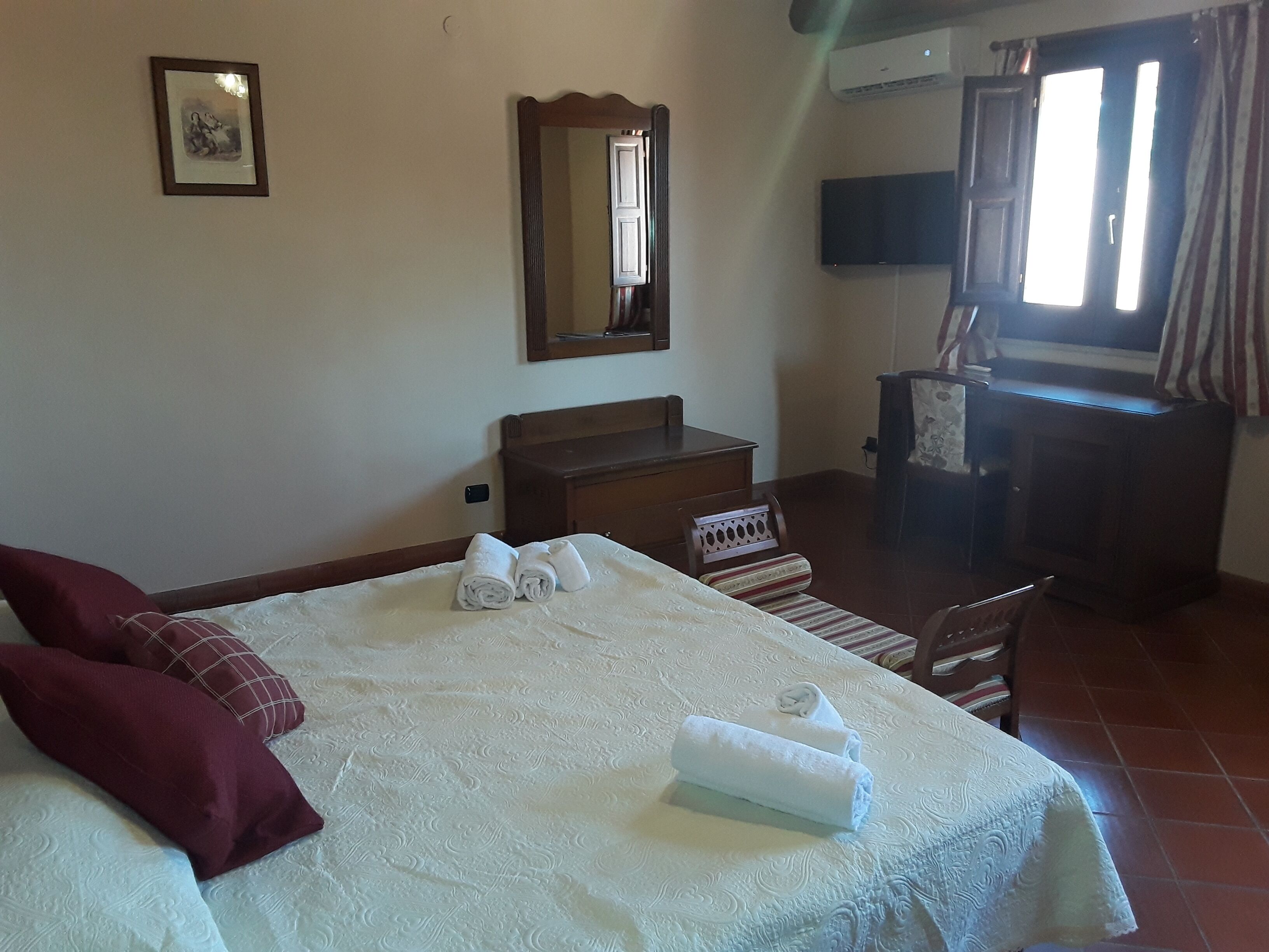 A hotel room with a bed, a wooden dresser, a mirror, a television, and a window with curtains.