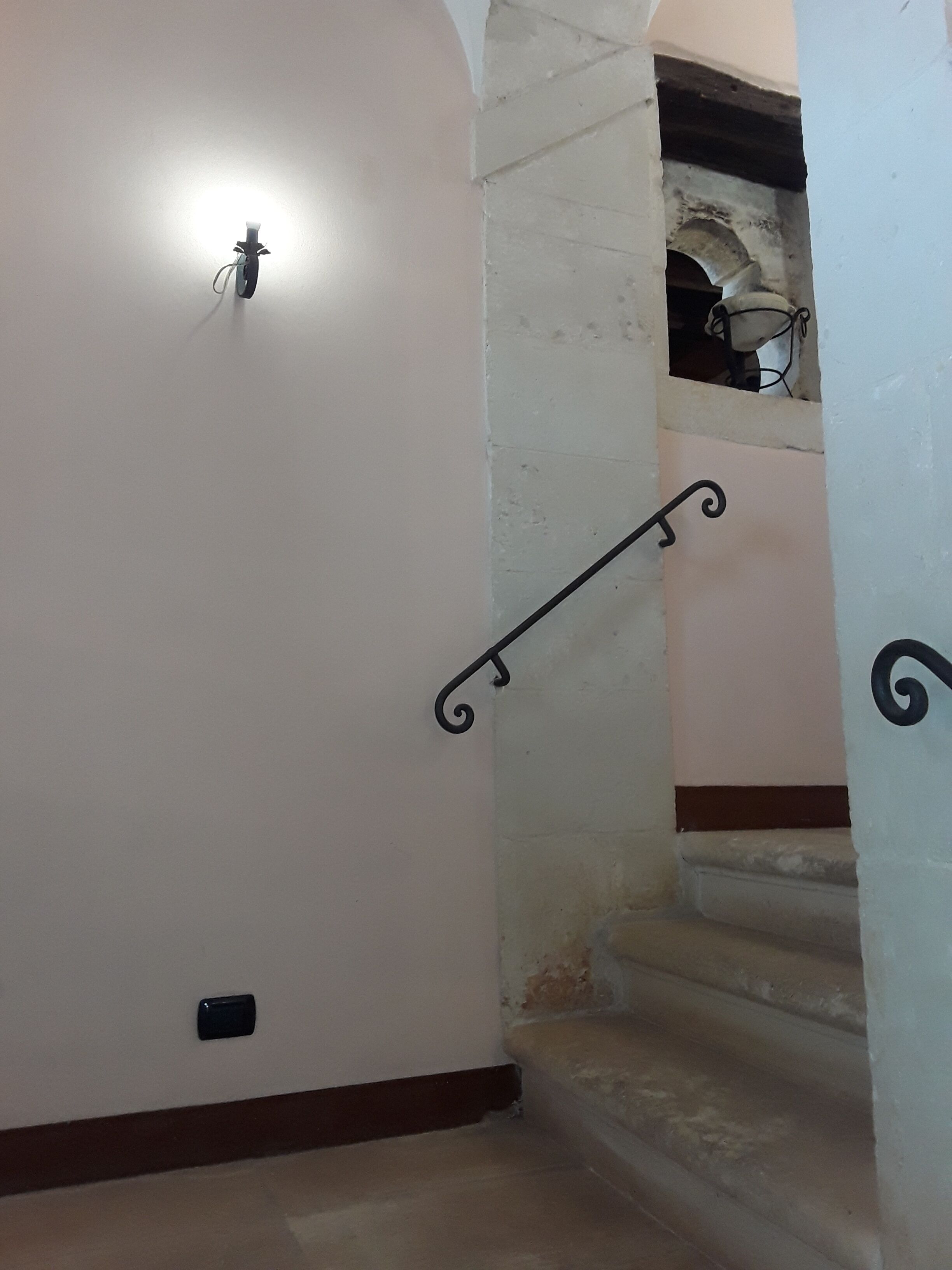 A staircase with a metal handrail, a light fixture on the wall, and a door with a small black object on the floor.