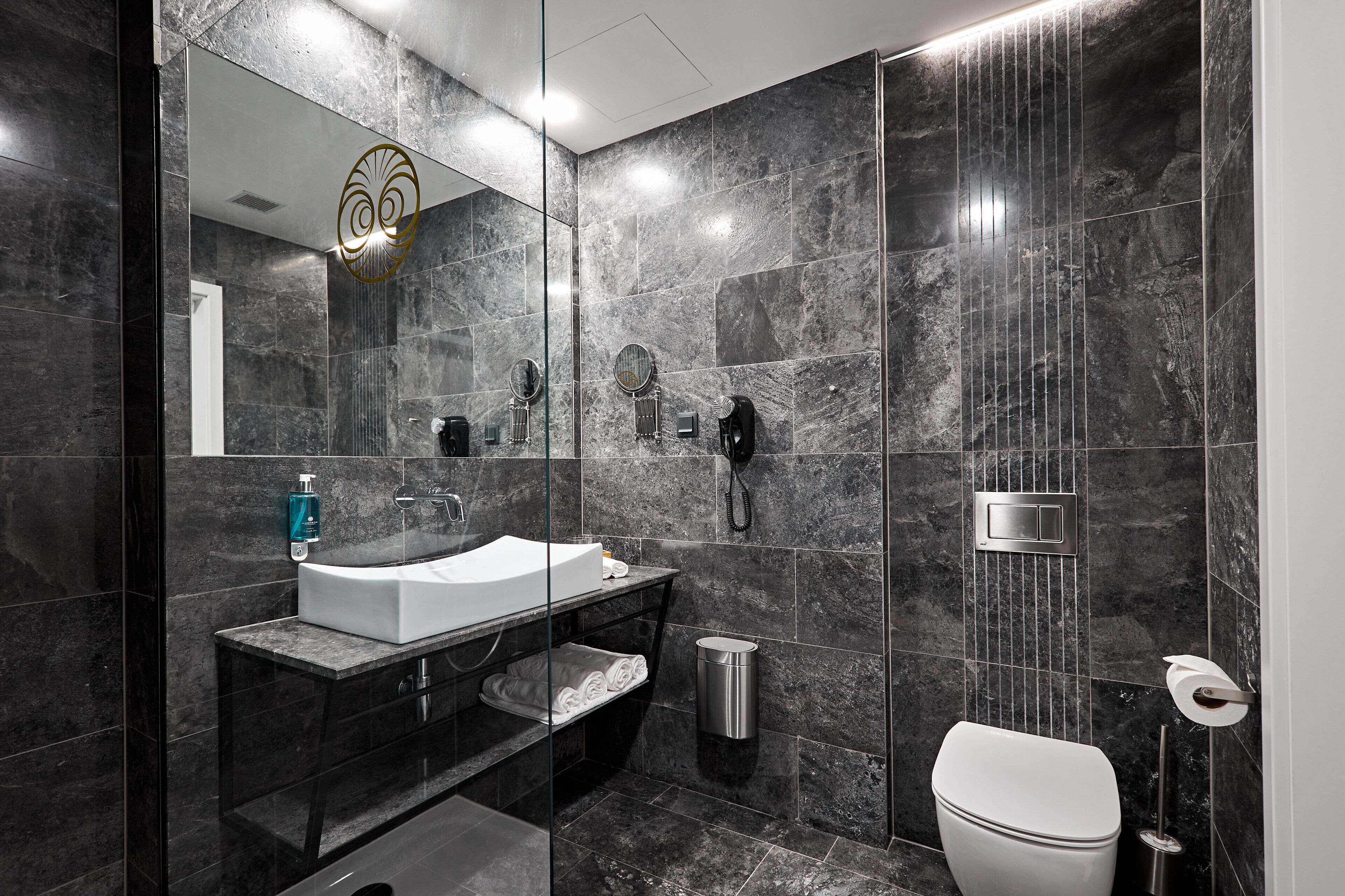 Un baño moderno con un espejo grande, un lavabo, un inodoro y una zona de ducha.