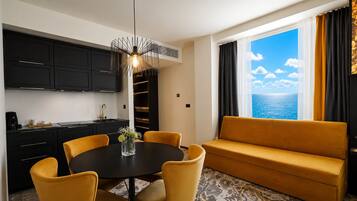 A modern hotel room with a dining area, a sofa, and a view of the sea.