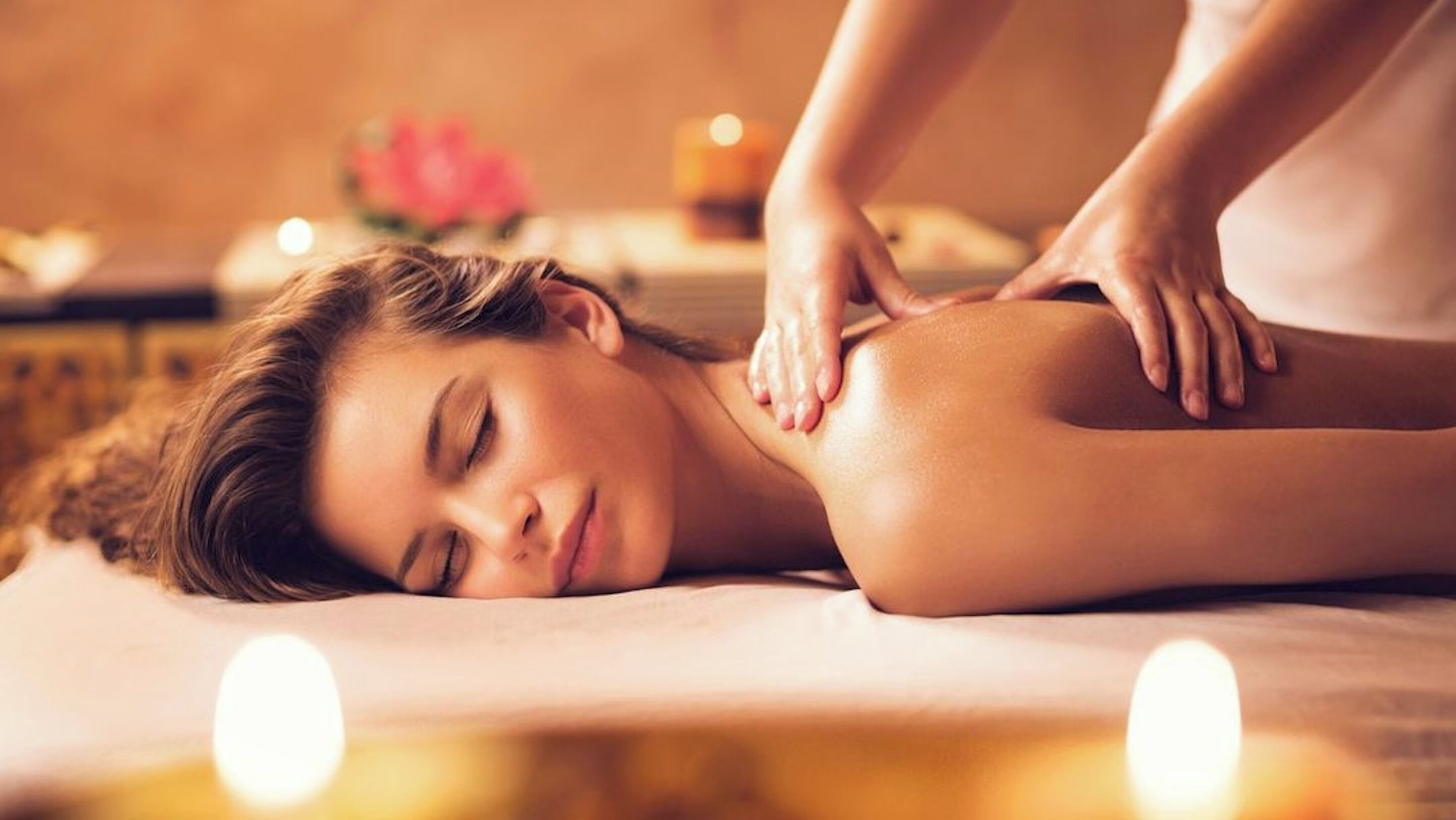A person receiving a massage in a spa setting with candles and a flower in the background.