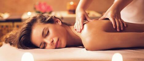 A person receiving a massage in a spa setting with candles and a flower in the background.