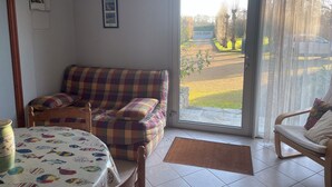 Un soggiorno con un divano a quadri, un tavolo da pranzo con tovaglia a motivi di pesce e vista su un giardino attraverso una porta vetrata.