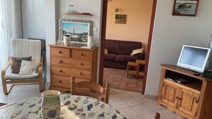 Un accogliente soggiorno con un mobiletto in legno, una televisione, un tavolo da pranzo con tovaglia a motivi di pesce e un divano.