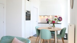 Une cuisine moderne avec des meubles blancs, une table à manger en bois, des chaises de couleur turquoise et un vase rempli de fleurs.