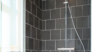 A shower area with a glass enclosure, black tiled walls, and a white bathtub. - De Torre 1 - luxury 1-bedroom apartment in iconic building (De Haan)