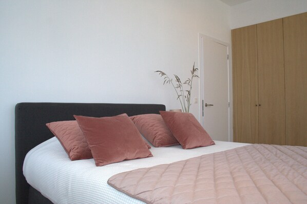 A bedroom with a bed, pillows, a bedside plant, and a wardrobe. - De Torre 1 - luxury 1-bedroom apartment in iconic building (De Haan)