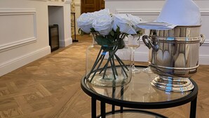 A glass table with a champagne bottle, a remote control, and white roses. - Domaine de la Trinité (Mauguio)