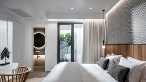 A modern bedroom with a large bed, a desk, and a bathroom.