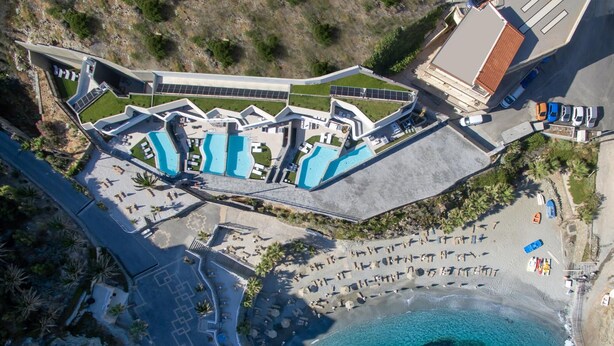 An aerial view of a resort with multiple swimming pools, a beach area, and a parking lot.