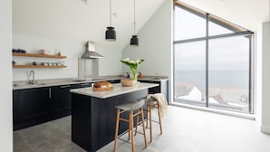 A modern kitchen with a large island, black cabinets, and a view of the sea. - The Old Coastguard Lookout (Port Isaac)