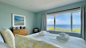 A bedroom with a large bed, a dresser, a chair, and a painting on the wall. - The Old Coastguard Lookout (Port Isaac)