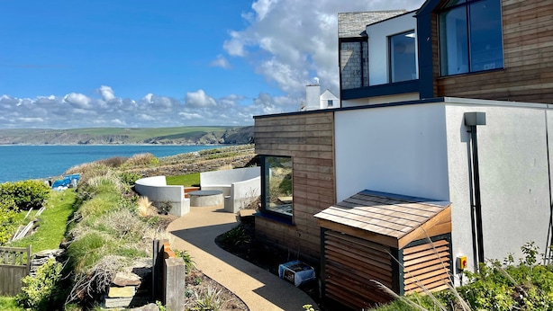A modern house with a large glass window, a wooden deck, and a view of the sea. - The Old Coastguard Lookout (Port Isaac)