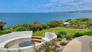 A landscaped garden with a circular concrete structure, a stone wall, and a view of the sea. - The Old Coastguard Lookout (Port Isaac)