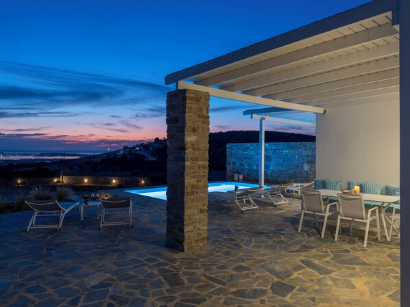 An outdoor patio with stone flooring, a pool, and lounge chairs.