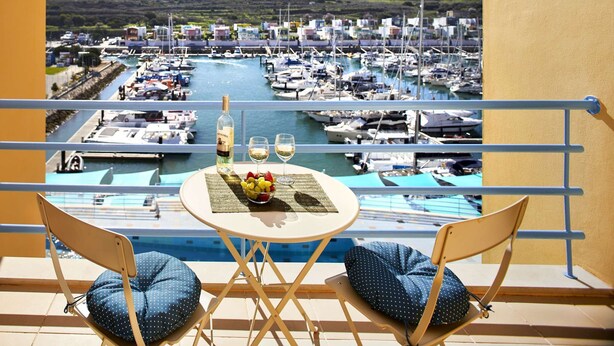 A balcony with two chairs and a table, overlooking a marina with numerous boats.