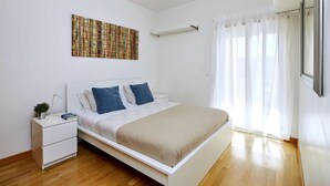A modern bedroom with a bed, white nightstands, a small plant, and a large abstract painting on the wall.