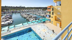 A marina with numerous boats docked, a swimming pool, and a yellow building with balconies.