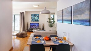 A modern dining area with a wooden table set for breakfast, a television in the background, and artwork on the walls. - Modern luxury apartment on the Albufeira Marina (Albufeira)