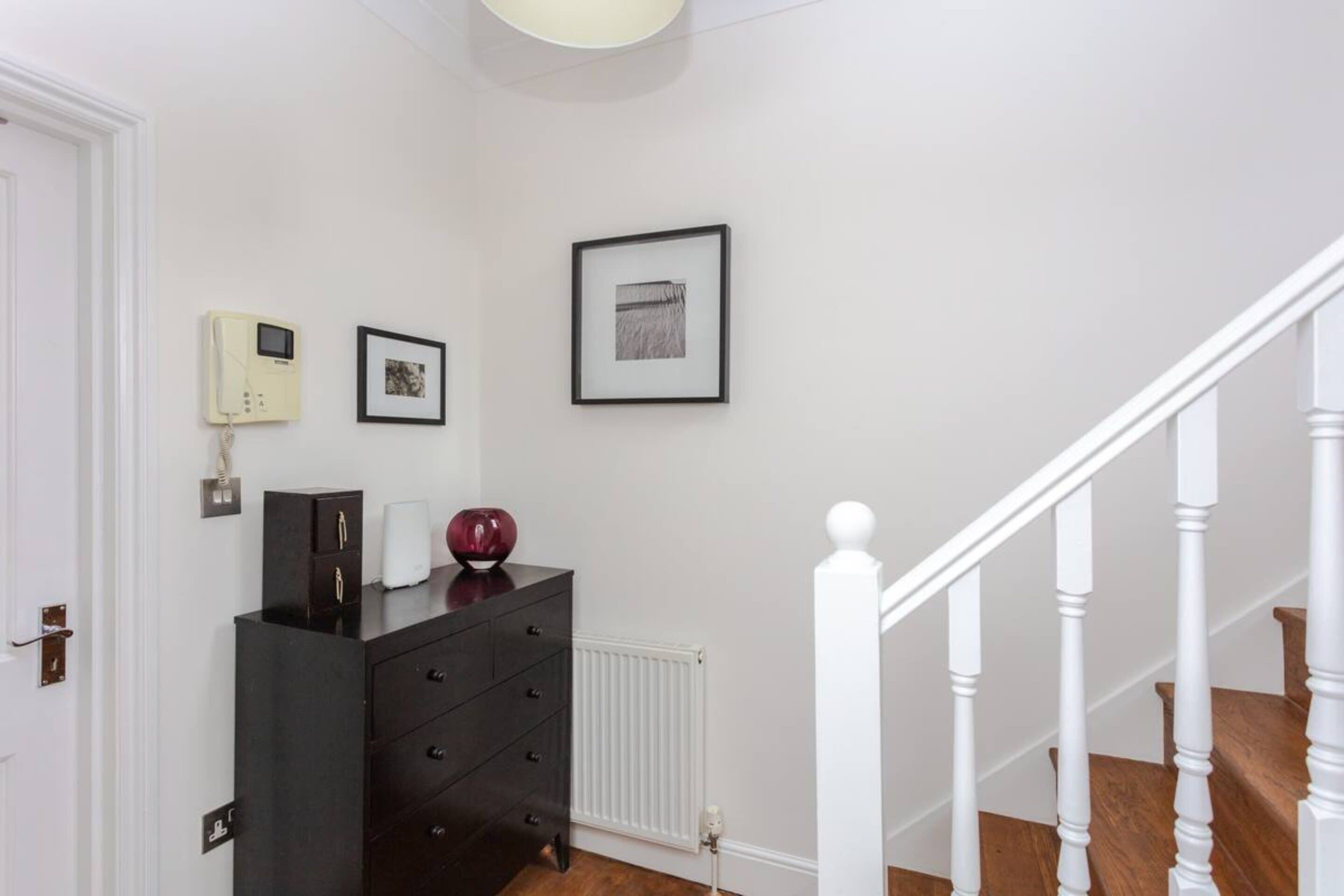 A hallway with a black dresser, a framed picture, and a white radiator.