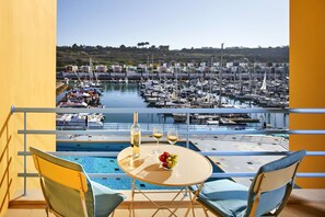 En balkon med poolbord, to stole og et bord med flaske og glas. En marina med både ses i baggrunden.